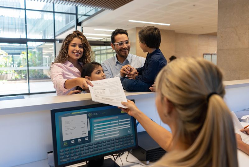 beautiful young mother with her kids and partner handing a form at the front desk of the hospital all smiling